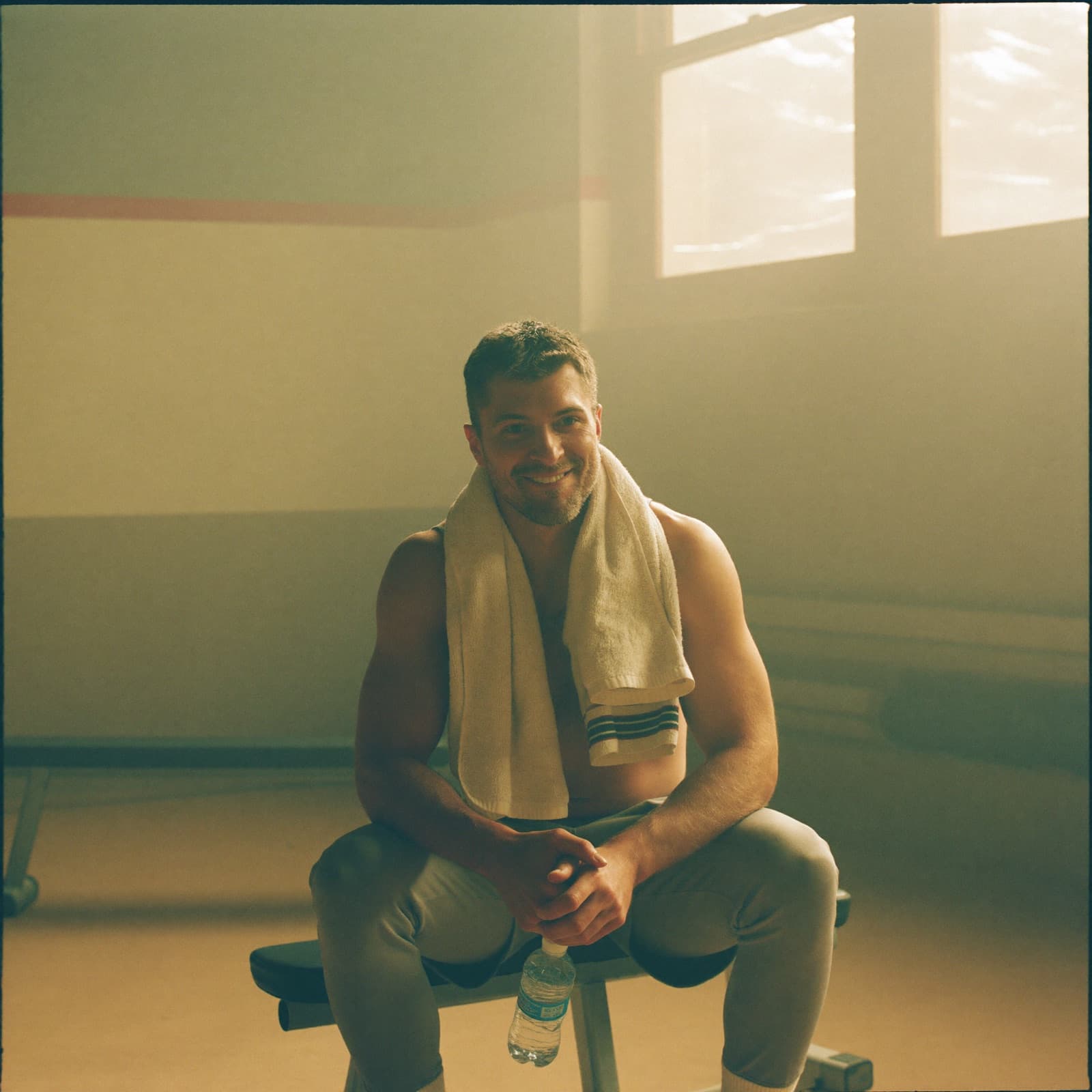 A lean man resting on a gym bench with a towel around his neck